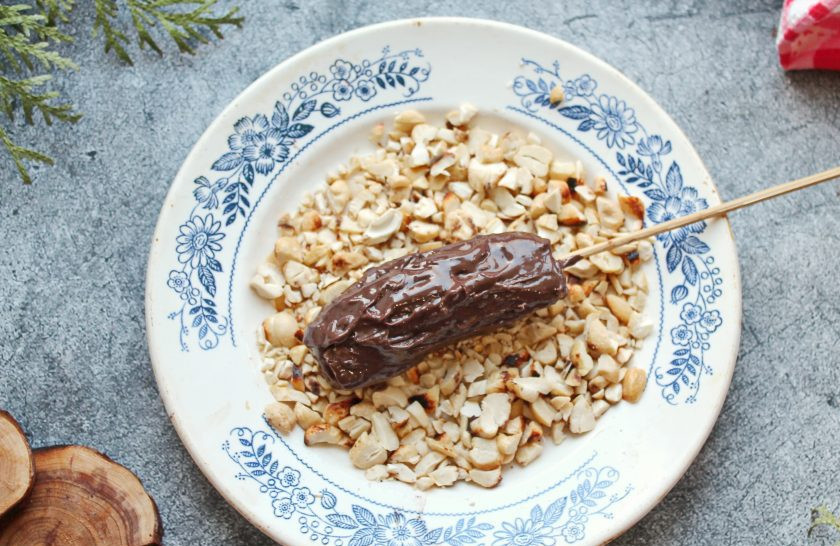 1. Этап. Банановый сникерс: Мини-бананы очистите от кожуры, немного срежьте со стороны изгиба, придавая ровную форму. Отрежьте кончики, чтобы получился брусочек. Нанизайте банан на деревянную шпажку и полностью покройте его шоколадно-ореховой пастой.