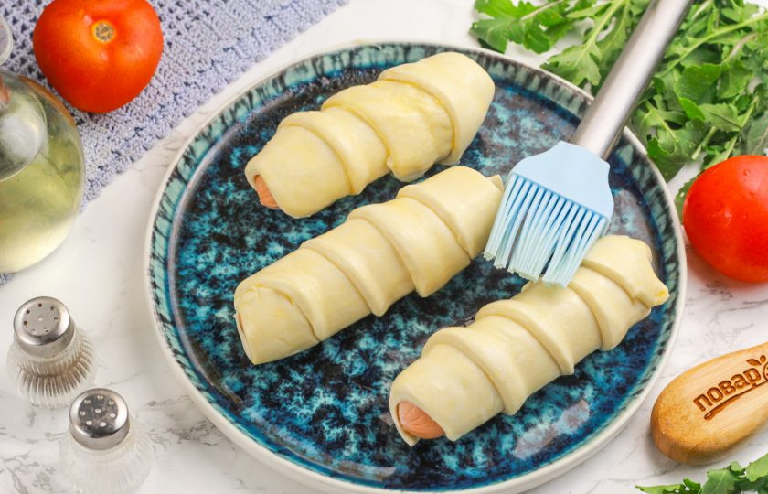 1. Этап. Сосиски в тесте в аэрогриле: Взбейте куриное яйцо и смажьте им с помощью кулинарной кисточки заготовки по длине.