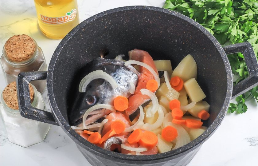 1. Этап. Уха из форели с рисом: Части рыбы выложите в кастрюлю или казан. Нарежьте очищенный картофель средними кубиками, лук — полукольцами, а морковь — кружочками. Выложите в емкость.