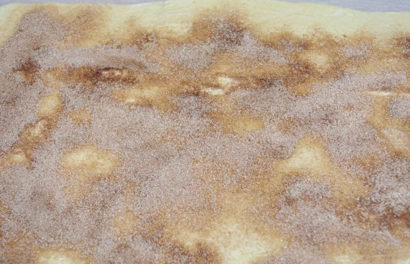 1. Этап. Булочки Синнабон: 9. Смажьте верхнюю часть пласта растопленным сливочным маслом. Используйте кисточку. Щедро посыпьте подготовленной коричной посыпкой.