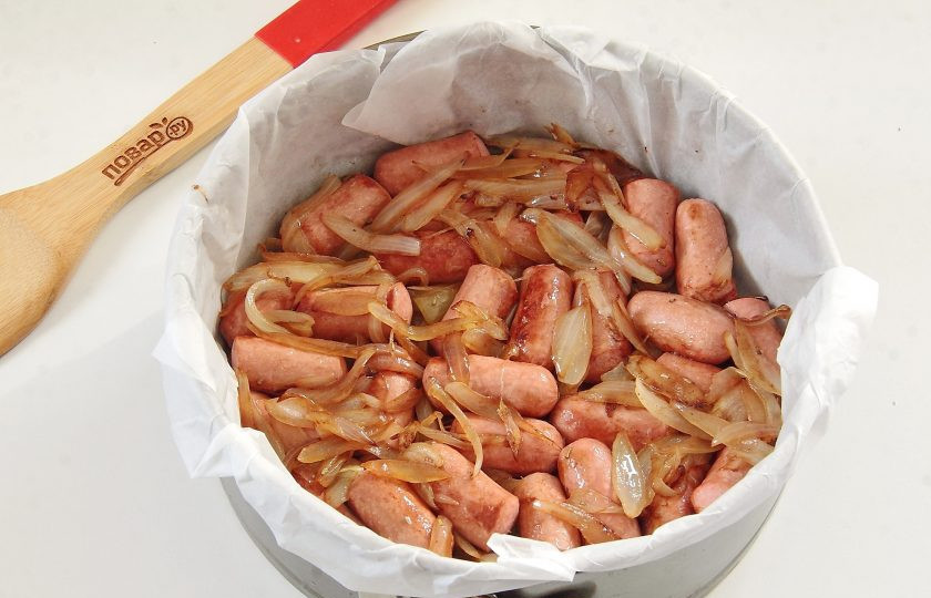 1. Этап. Пирог с колбасками и карамелизированным луком: Форму застелите пекарской бумагой (размером не более 22 см в диаметре) и положите на дно колбаски с луком.