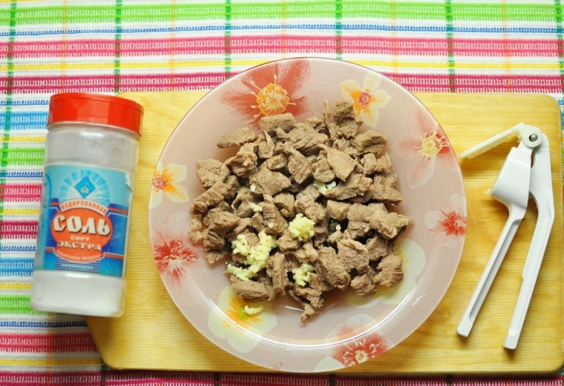 1. Этап. Салат с говядиной и корейской морковкой: Обжаренное мясо снимите с огня, выдавите в него чеснок. Перемешайте и обязательно посолите.