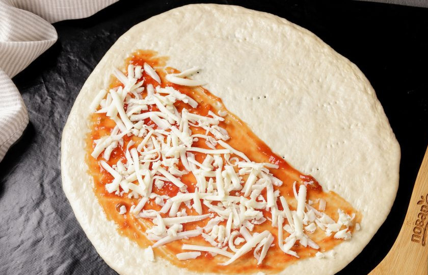 1. Этап. Пицца Кальцоне: Посыпьте соус частью тёртого сыра. Подойдёт любой, который хорошо плавится, у меня сегодня сулугуни.