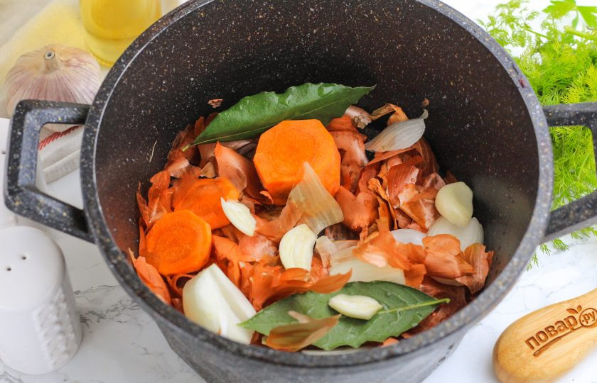 1. Этап. Щековина свиная в луковой шелухе: Несколько раз промойте в воде луковую шелуху, чтобы удалить пыль и прочий мусор. Выложите ее в казан вместе с очищенной морковью, луком и чесночными зубчиками. Добавьте лавровые листья.