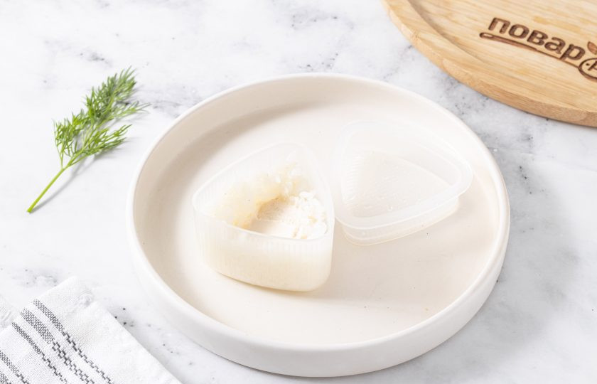 1. Этап. Онигири с огурцом: Смочите руки и формочку для онигири водой. Заполните форму наполовину, сделав углубление для начинки. В центр выложите немного сливочного сыра.