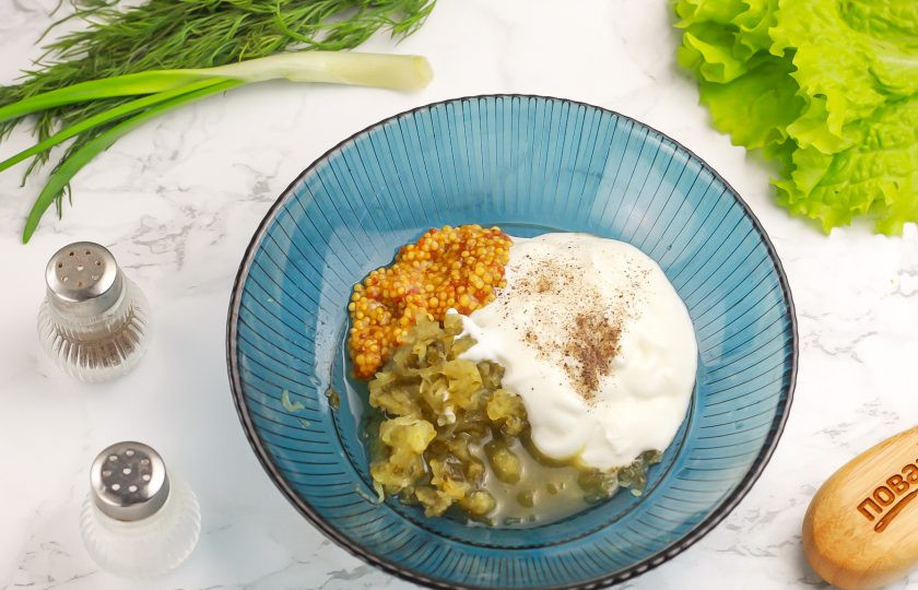 1. Этап. Салат Тёщин: В это время натрите соленый огурец на терке с мелкими ячейками в пиалу или креманку. Добавьте сметану любой жирности, лимонный сок, зерновую горчицу и молотый черный перец. Тщательно перемешайте, получая салатную заправку.