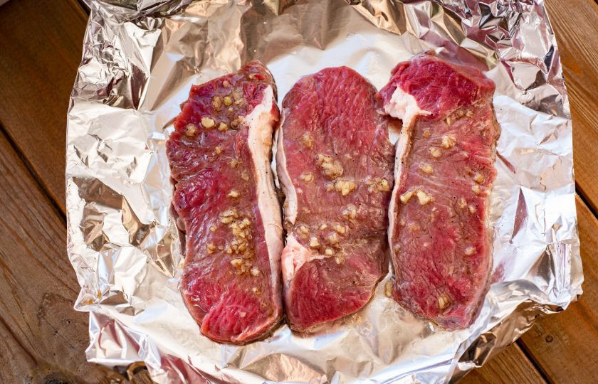 1. Этап. Антрекот в аэрогриле: Сложите в два слоя пищевую фольгу, чуть поднимая края, и выложите поверх замаринованные куски говядины вместе с маринадом.