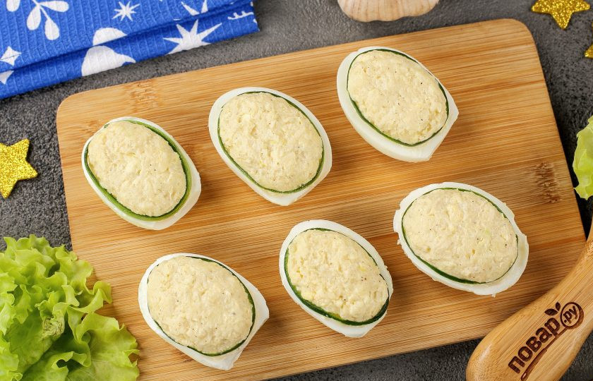 1. Этап. Фаршированные яйца Глаз дракона: При помощи овощечистки срежьте с огурца тонким слоем кожуру и нарежьте на тонкие полоски. По периметру фаршированной сырно-желтковой массы выложите полоски огурчика.