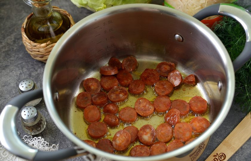 1. Этап. Капустняк по-польски со свежей и квашеной капустой: В кастрюлю с толстым дном влейте немного растительного масла, колбаски почистите от оболочки, нарежьте кружочками, обжарьте несколько минут.