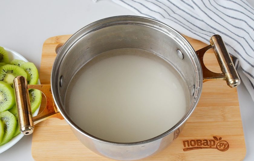 1. Этап. Цукаты из киви: В подходящую по размеру кастрюльку всыпьте сахар и влейте воду. Доведите до кипения, проварите 1 минутку.