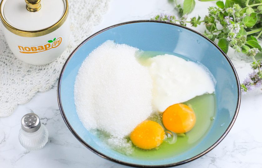 1. Этап. Кокосовые кексы: Вбейте куриные яйца в глубокую емкость, всыпьте соль, сахарный песок и добавьте сметану любой жирности. Взбейте все венчиком примерно 2-3 минуты. Не нужно взбивать в пышную пену, достаточно качественно перемешать с сахаром и сметаной.