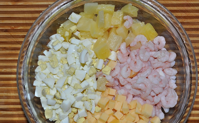 1. Этап. Салат из креветок и ананасов: Нарежьте кубиками сыр, натрите на терке яйца, порежьте кубиками ананасы. Соберите все в салатнице, добавив креветки.