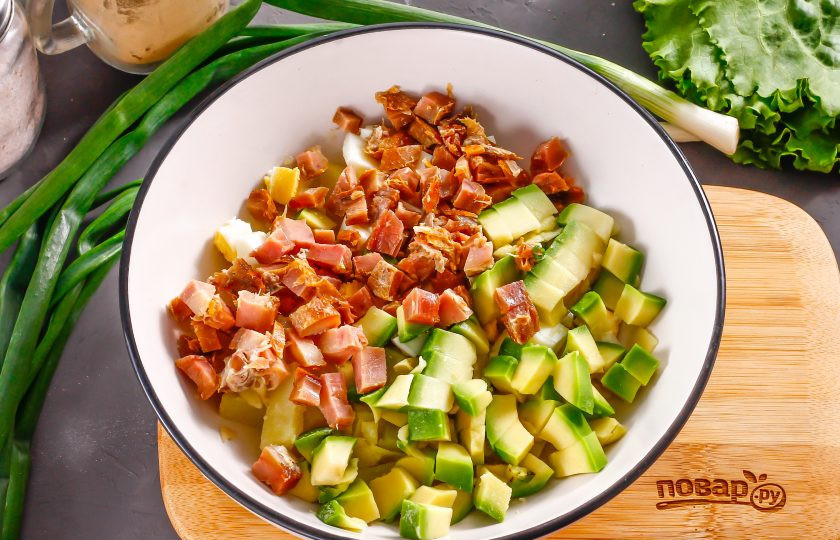 1. Этап. Салат с копченой курицей и авокадо: Нарежьте кубиками мясо копченой курицы: грудинку, филе, мякоть с окорочков и т.д. Удалите ядро у авокадо, счистите кожуру и нарежьте мякоть кубиками. Добавьте в емкость вместе с нарезкой курицы.