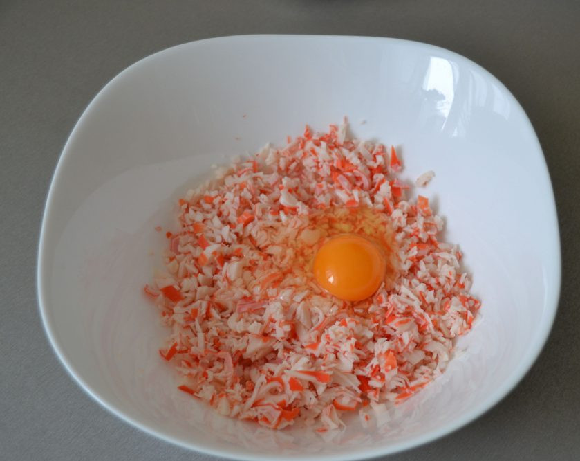 1. Этап. Драники с крабовыми палочками: Измельчите крабовые палочки, вбейте 1 яйцо.