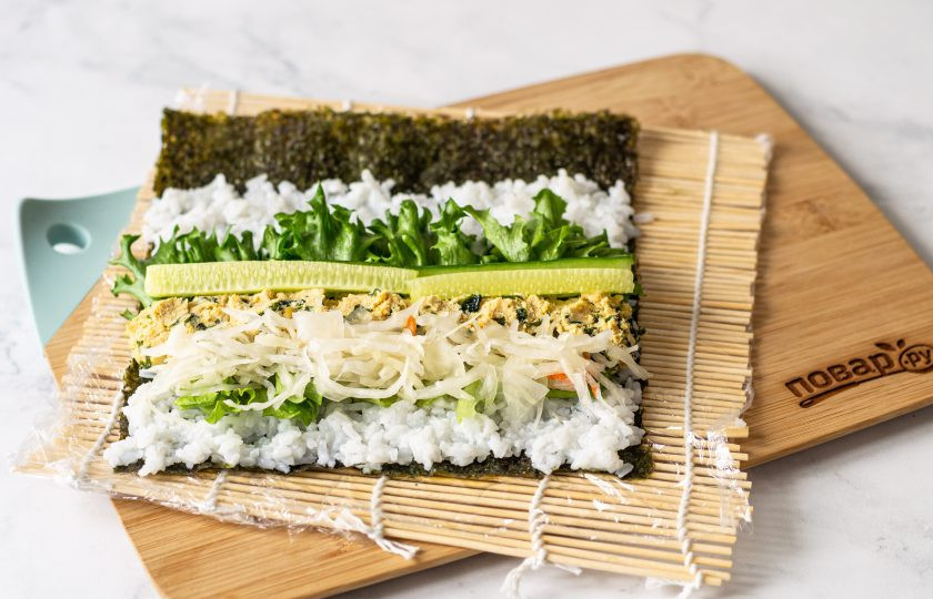 1. Этап. Роллы Эхо-маки: Выложите на циновку лист нори шершавой стороной вниз. Сверху выложите тонким слоем рис, отступив с одного края пару сантиметров. На рис в центр выложите начинку из листьев салата, нута, квашеной капусты и огурца. Закрутите ролл, смочите свободный край водой и закрепите.