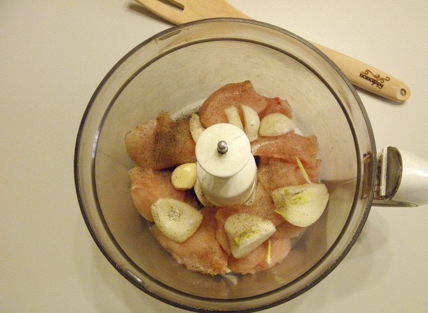1. Этап. Котлетки из куриных грудок: Отделите куриное мясо от кости, снимите и выбросьте шкуру. Сложите в измельчитель мясо, лук и чеснок. Добавьте по вкусу соль и щепотку молотого перца.