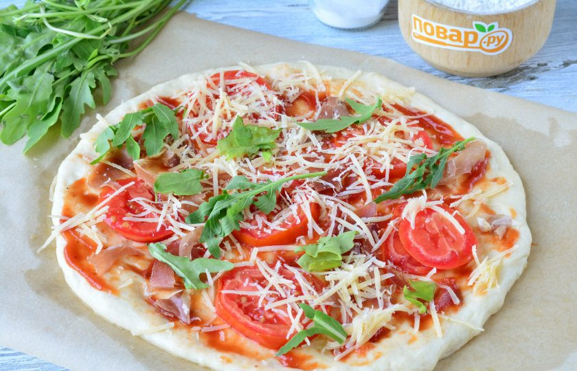 1. Этап. Пицца с прошутто и рукколой: Присыпьте пиццу натертым сыром. Добавьте половину порции рукколы. Оставьте немного свежей рукколы для подачи.