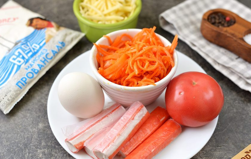 1. Этап. Салат из крабовых палочек, моркови по-корейски и сыра: Подготовьте ингредиенты. Крабовые палочки заранее разморозьте, отварите яйцо не дольше 10 минут, остудите в ледяной воде, натрите твердый сыр, помойте и обсушите помидор.