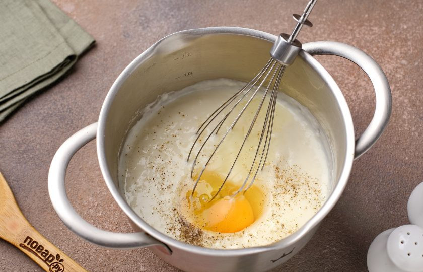 1. Этап. Запеканка Южная с кабачками и помидорами: Дайте соусу немного остыть, посолите, поперчите и добавьте яйцо. Хорошенько взбейте.