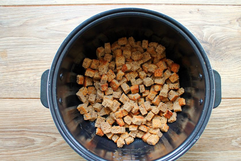 1. Этап. Сухарики в мультиварке: У хлеба отрежьте корки и порежьте его на одинаковые квадратики. Выложите их в сухую чашу мультиварки и включите в рабочий режим. Обжаривайте хлеб, перемешивая, до подсушивания и золотистого цвета.