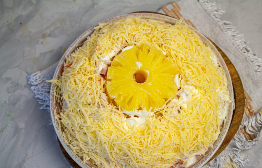 1. Этап. Салат Ананасовое кольцо: Натрите сыр на мелкой терке и посыпьте всю поверхность салата, за исключением ананасовых колечек.