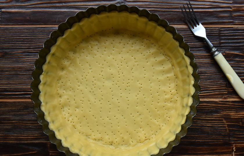 1. Этап. Пирог Ложный сырник: Достаньте из холодильника часть теста и раскатайте его в пласт, толщиной 0,5-0,7 мм. Перенесите тесто в форму для выпекания и распределите по дну и бортам. Наколите тесто вилкой, чтобы избежать деформации при выпекании.