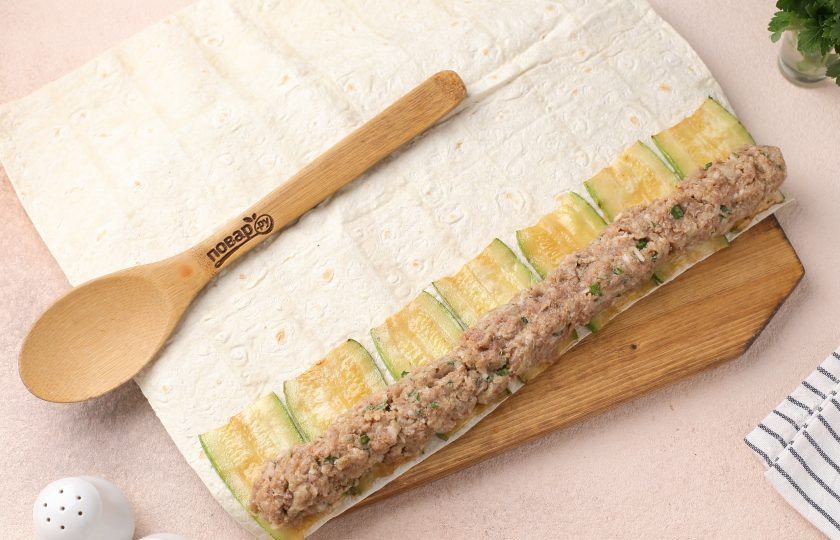 1. Этап. Пирог из лаваша с фаршем и кабачком: На один край лаваша выложите в один ряд обжаренные кабачки. Затем из фарша сформируйте колбасу и выложите её сверху. Начиная со стороны кабачков с фаршем, плотно сверните лаваш в рулет.