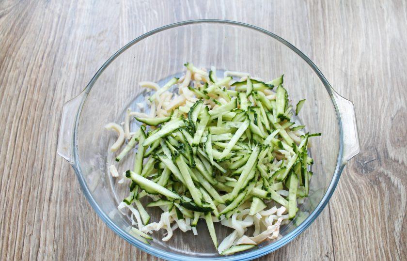 1. Этап. Салат Морской волк: Огурец вымойте, обсушите и порежьте соломкой. Выложите огурец в миску с кальмарами.