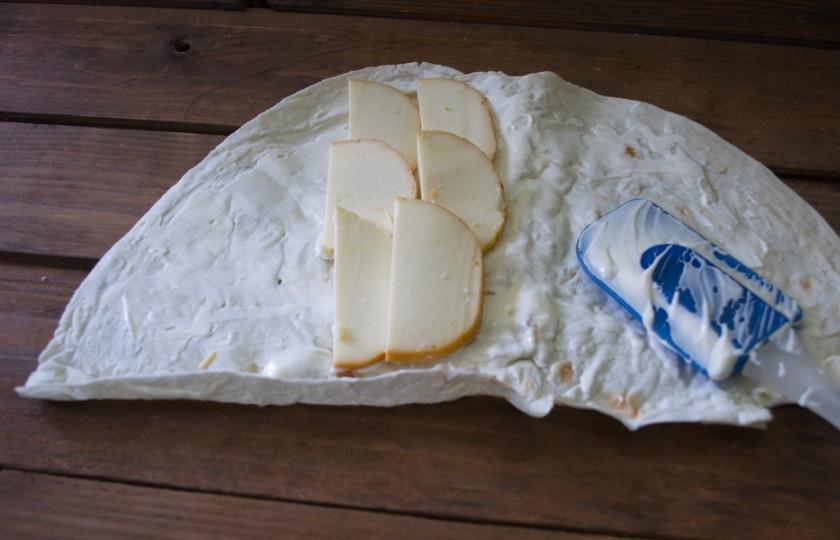 1. Этап. Лаваш с копченым сыром: На серединку лаваша выложите нарезанный сыр. Форма нарезки зависит от упаковки сыра. Мой круглый. Нарезала тонко, плоскими полукольцами.