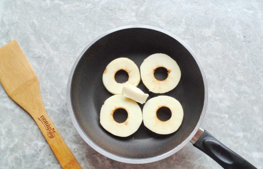 1. Этап. Шницель из свинины с яблоком: Яблоко вымойте, очистите, удалите сердцевину. Нарежьте кольцами. Выложите на сковороду и добавьте сливочное масло.