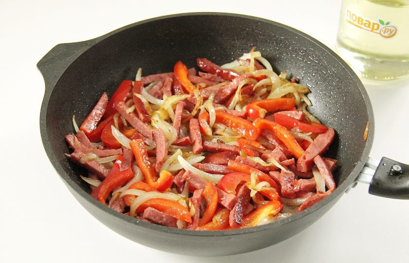 1. Этап. Картофель с копченой колбасой: Разогреваем на сковороде растительное масло и обжариваем лук до готовности, добавляем колбасу и даем ей подрумяниться. Затем добавляем перец и жарим все вместе еще 2-3 минуты.