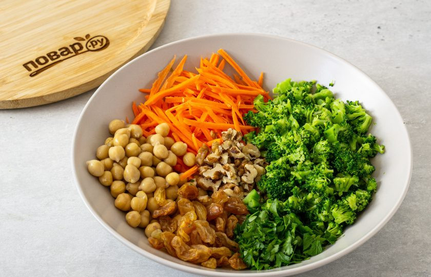 1. Этап. Салат из нута с брокколи: Мелко нарежьте брокколи. Морковь очистите и натрите на терке для моркови по-корейски. Петрушку и грецкие орехи мелко порубите. Консервированный нут промойте, откиньте на сито и дайте стечь жидкости. Изюм промойте, обсушите. Переложите все ингредиенты в глубокую миску.