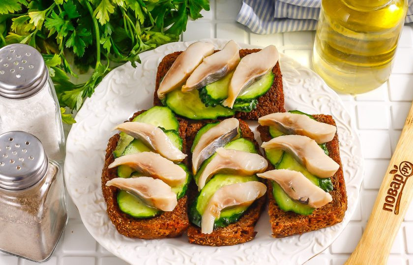 1. Этап. Тосты с селедкой: Выложите ломтики сельди на огурцы. Сверху можете полить селедочным маслом, если приобретали сельдь в пресерве. Ни майонез, ни сметану использовать не нужно.