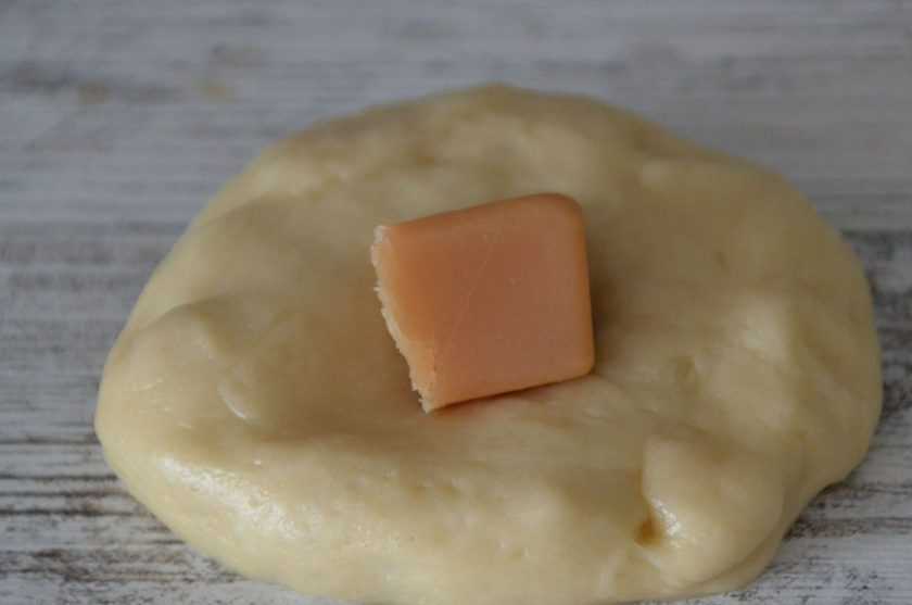 1. Этап. Булочки с конфетами Коровка: Расплющите ладонью тесто, в центр лепешки выложите половинку конфеты, защипните края, переверните швом вниз и подкатайте в шар.