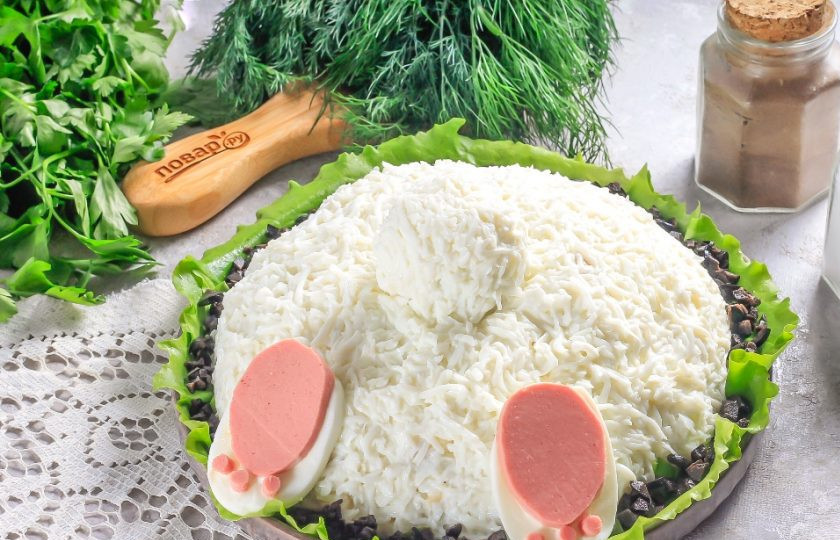 1. Этап. Салат с ананасами на Новый год Кролика 2023: На оставшийся желток выложите оставшуюся белковую массу и округлите в руках, выложите поверх горки салата — это хвостик. Целое яйцо нарежьте кружочками. Два крупных из них выложите на салат. Вырежьте из вареной колбасы пяточки с помощью ножа, а подушечки сделайте с помощью трубочки для коктейлей. Приклейте к яйцу на майонез. Салатные листы промойте, срежьте с них кружевные бока и выложите вокруг салата. Измельчите маслины без косточек и присыпьте вокруг салата, нарезка будет символизировать землю, в которую зарылся кролик.