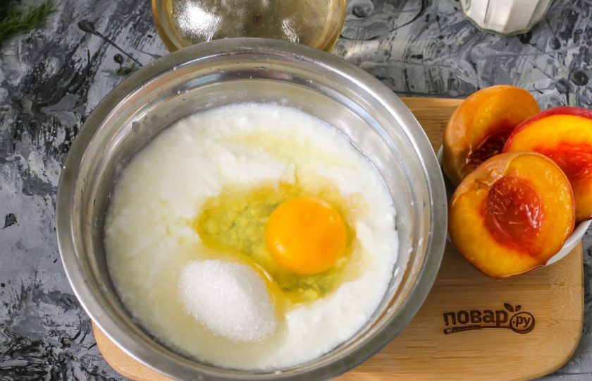 1. Этап. Оладьи на кефире с персиками: Кефир любой жирности влейте в глубокую емкость, вбейте туда же куриное яйцо. Всыпьте сахарный песок и соль, взбейте.