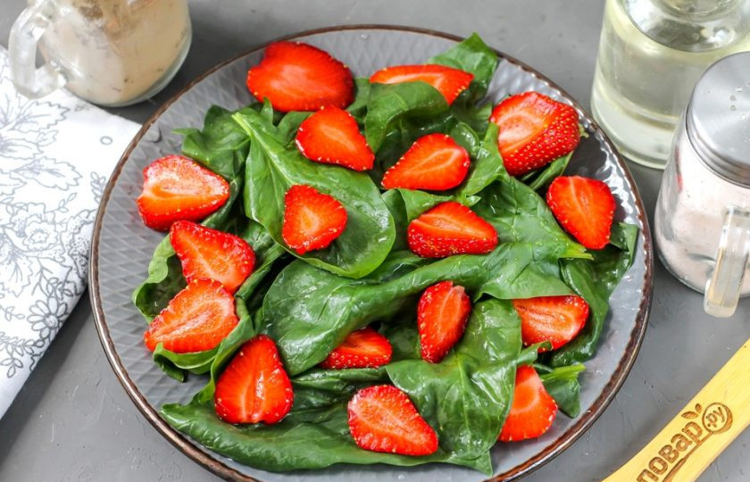 1. Этап. Шпинат с клубникой и орехами: Клубнику промойте в воде и удалите с ягод хвостики. Разрежьте каждую из них пополам или на четыре части, выложите на шпинат.