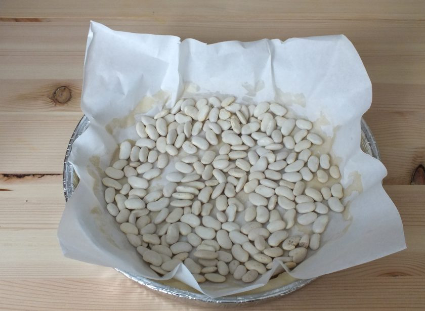 1. Этап. Пирог с черносливом и сметаной: На тесто положите пищевой пергамент и насыпьте сверху фасоль или нут. Разогрейте духовку до 180 градусов. Поставьте форму с тестом в духовку и выпекайте 15-20 минут, до легкого румянца бортиков теста.