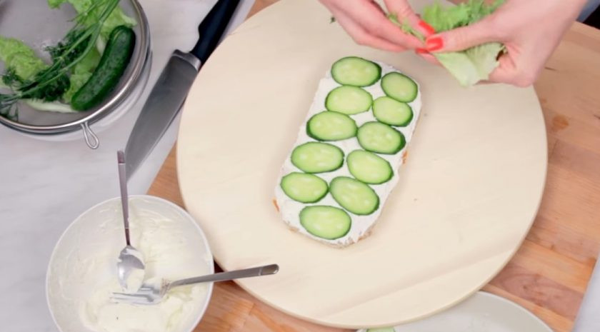 1. Этап. Сэндвич-торт Джейк из Время приключений: 4. Выложите слой нарезанной рыбы и укроп, прикройте вторым слоем хлеба, смазав его заправкой. На второй слой хлеба выложите нарезанные огурцы и листья салата, прикройте третьим слоем хлеба.