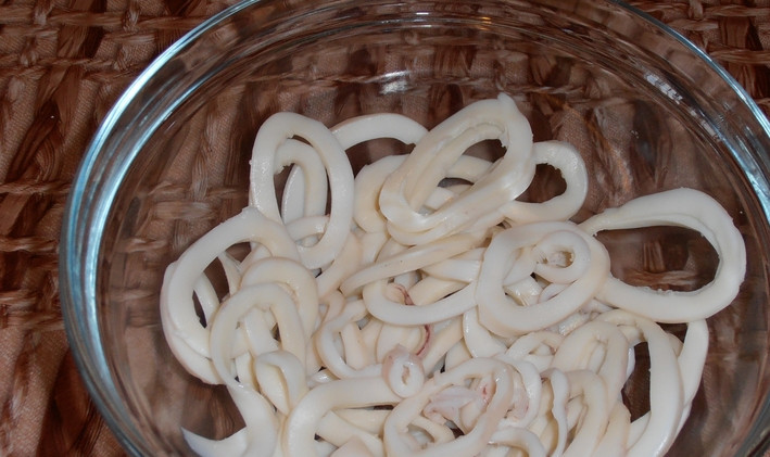 1. Этап. Новогодний салат из кальмаров: Кальмары очищаем и отвариваем в подсоленной воде 5 минут. Даем кальмарам остыть и нарезаем их колечками, которые складываем в салатницу