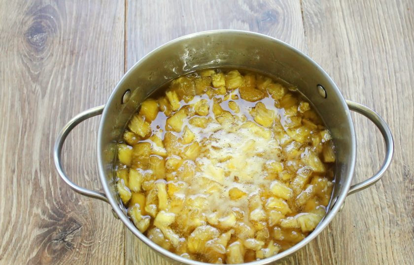 1. Этап. Ананасы на зиму: Достаньте кастрюлю с ананасами, перемешайте. Фрукт должен выделить достаточно много сока, если этого не произошло, влейте 100 миллилитров холодной воды. Поставьте кастрюлю на средний огонь и доведите до кипения. Варите ананасы в течение 5 минут, снимая пену, если такая будет образовываться. Снимите с огня и дайте заготовке полностью остыть.