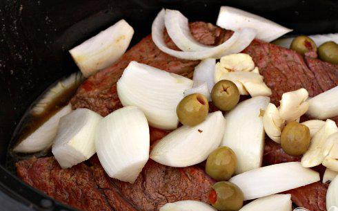 1. Этап. Говядина с кукурузными лепешками: 2. Нарезать луковицу и мелко нарезать чеснок. Очистить и нарезать морковь. Залить мясным бульоном говядину, добавить софрито и томатную пасту. Поставить на медленноварку. Добавить лук, чеснок и душистый перец с оливками к мясу. Готовить на низком уровне в течение 10 часов или на высоком уровне 6 часов. За 2 часа до готовности добавить морковь и помидоры.