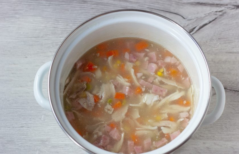 1. Этап. Аспик из курицы и овощей: Нагрейте бульон на медленном огне и помешивайте до полного растворения желатина. Доводить до кипения не нужно. Когда желатин растворится, добавьте в бульон курицу, ветчину, морковь, горошек и кукурузу. Перемешайте.