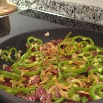 1. Этап. Рыба по-испански: Выложить в сковороду с луком и чесноком нашинкованный кольцами сладкий перец и порезанную ломтиками чоризо. Перемешать.