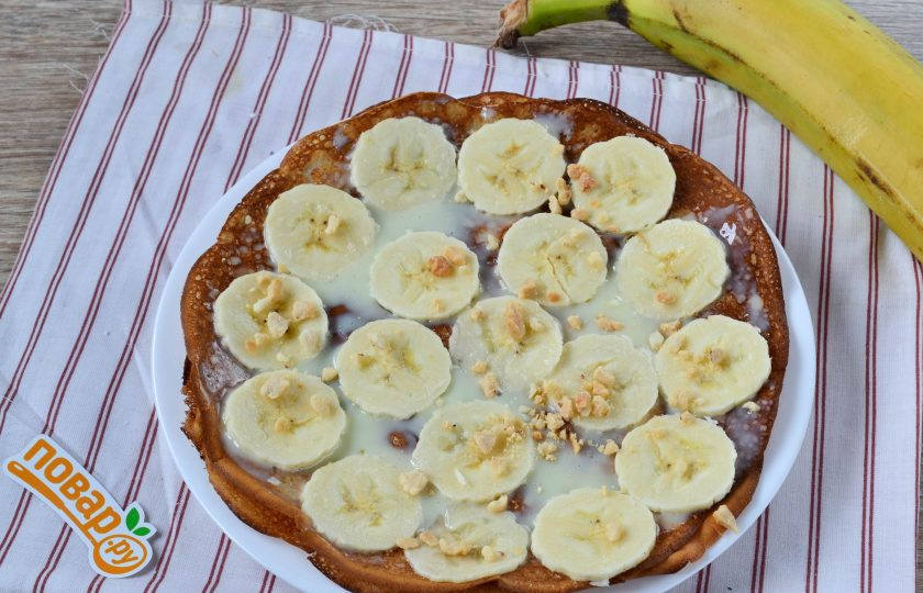 1. Этап. Блинный торт с грецкими орехами и бананами: 8. Начинаем формировать торт. На плоскую тарелку положите первый блин, смажьте его сгущенкой, выложите тонкие кружочки банана и присыпьте измельченными грецкими орехами (можно использовать и другие орехи).