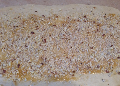 1. Этап. Булочки с медом: Слегка смажем стол или разделочную доску растительным маслом и раскатаем тесто в прямоугольный пласт толщиной 6-7 мм. Смазываем жидким (!!!) медом и посыпаем орехами. Если у вас густой мед, растопите его на водяной бане.