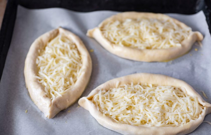 1. Этап. Хачапури по-аджарски на кефире: Выложите лодочки с сыром на противень, застеленный пергаментом для выпечки — выпекайте в уже разогретой до 180 градусов духовке в течение 20 минут. Затем достаньте противень с хачапури из духовки и на поверхность каждой лодочки аккуратно вбейте яйцо, отправьте вновь противень в духовку и готовьте еще 5 минут — яйцо должно запечься.