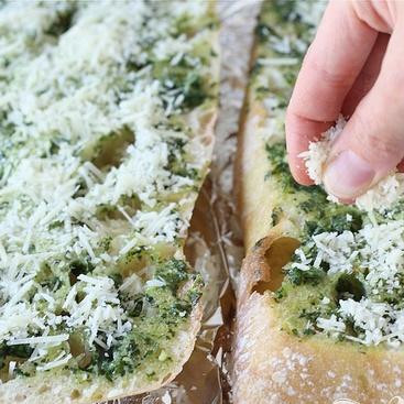 1. Этап. Бутерброды с базиликовым маслом: 4. Достать хлеб из духовки, разделить половинки и посыпать каждую тертым сыром Пармезан. Вернуть половинки обратно в духовку, увеличить огонь до 260 градусов и выпекать хлеб до тех пор, пока сыр полностью не расплавится, половинки хлеба не станут золотисто-коричневого цвета.