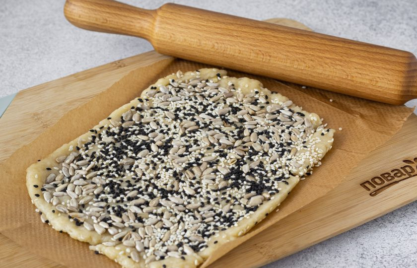 1. Этап. Печенье с семечками подсолнуха и кунжутом: Раскатайте тесто толщиной 5-6 мм. Сверху посыпьте кунжутом и подсолнечными семечками. С помощью скалки вдавите их в тесто.