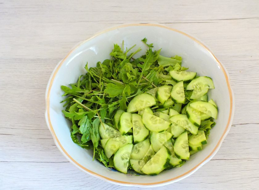 1. Этап. Салат с крабовыми палочками и рукколой: С огурца снимите кожуру, нарежьте тонкими ломтиками. Переложите в салатник.